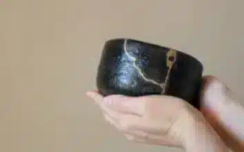Twee handen houden een kom vast die herstelt werd volgens de kintsugi methode