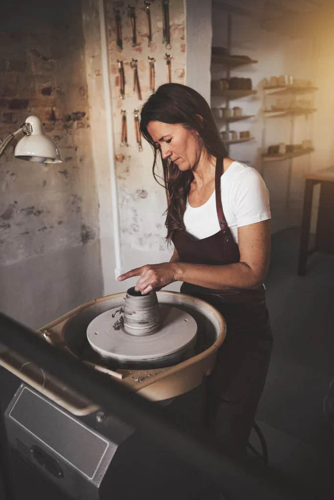 Klei mengen: keramiste aan de draaischijf draait een pot van gemengde klei af