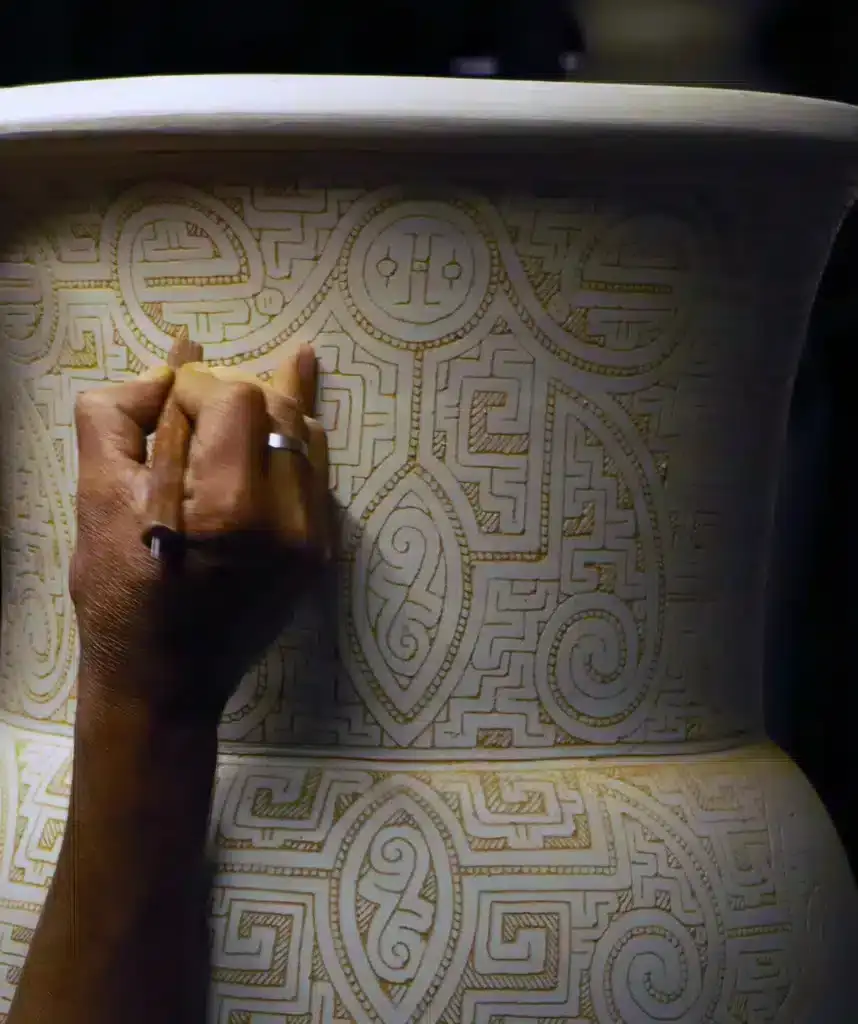 Een hand die met de sgraffito techniek een hele grote pot van keramiek decoreert