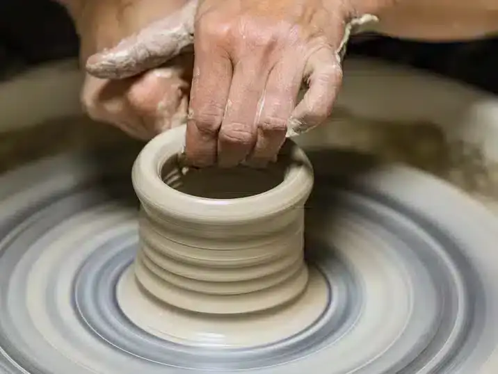 Twee handen die klei optrekken op de draaischijf, misbaksels en kleikrimp