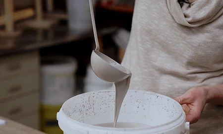 Een pollepel met grijs glazuur die stroomt in een emmer