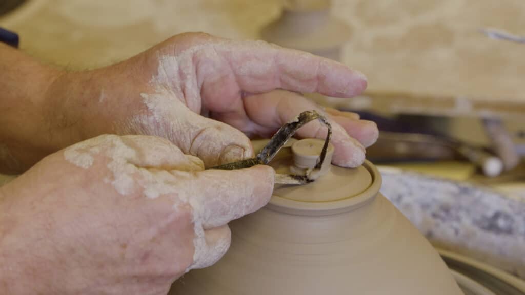 Theepot maken: twee handen draaien een dekseltje van een pot af op de draaischijf