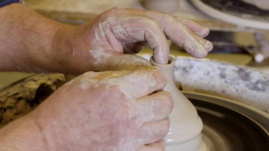 Theepot cursus: twee handen vormen een teutje van klei op de draaischijf