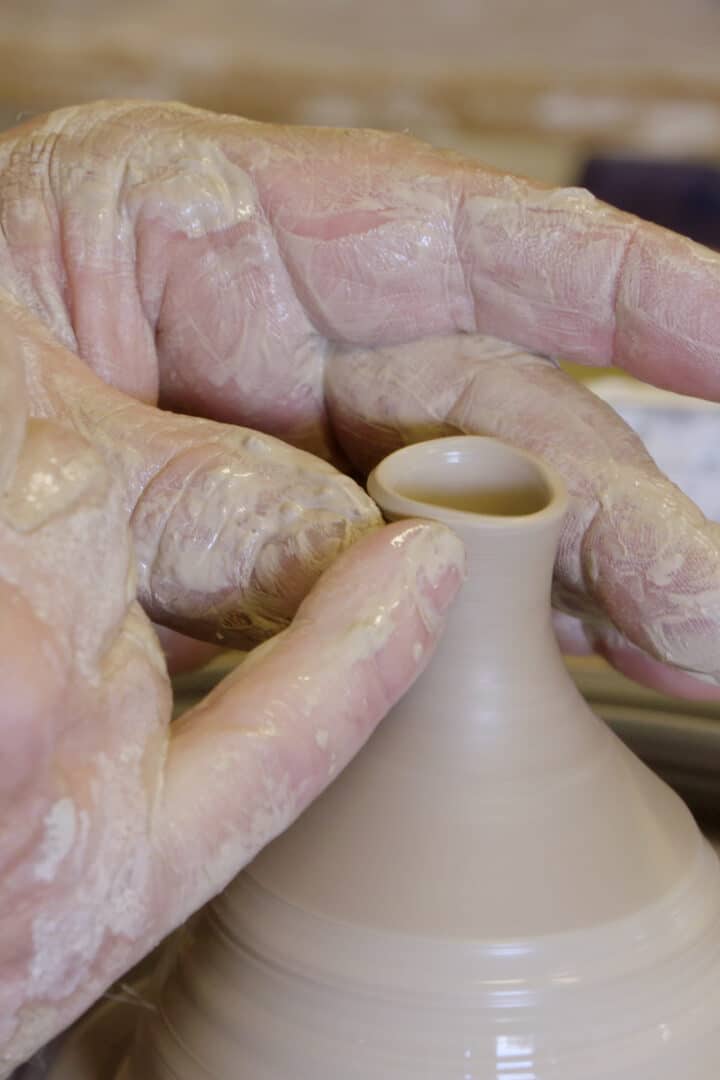 Twee handen vormen een teutje van klei op de draaischijf