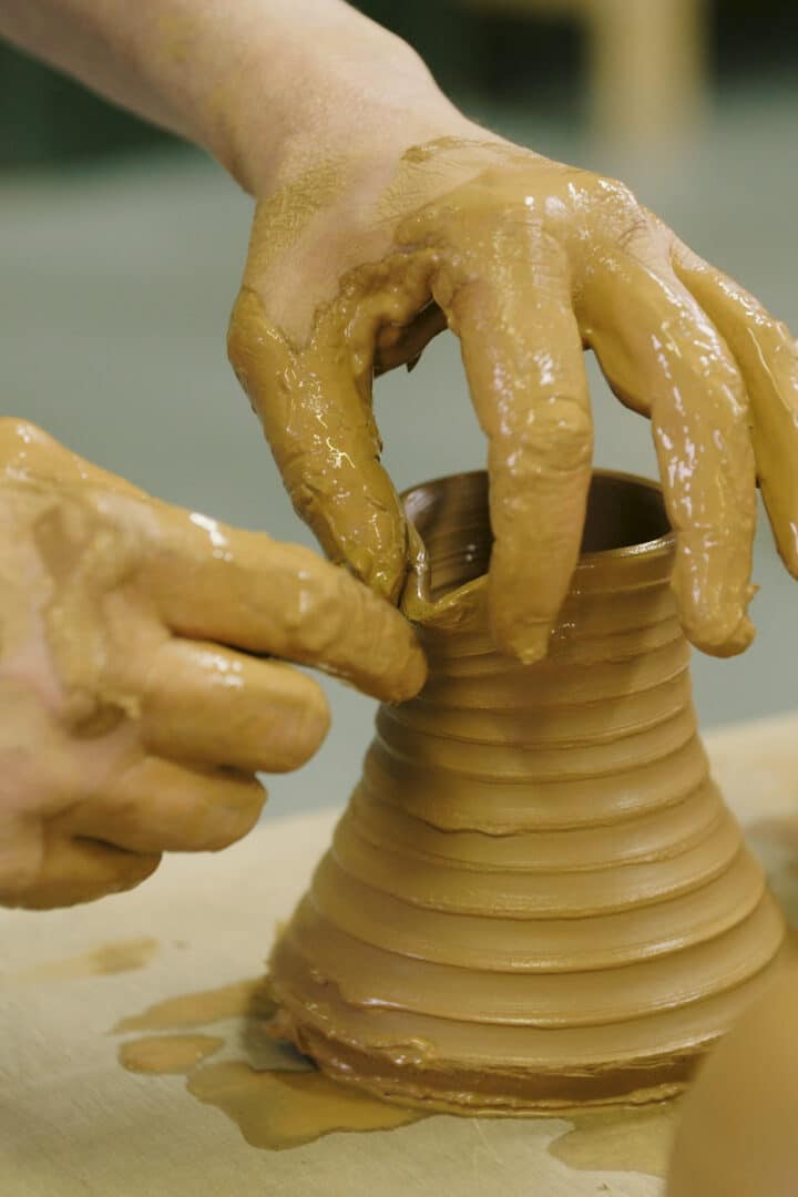 Twee handen maken een teutje aan een hoog smal potje