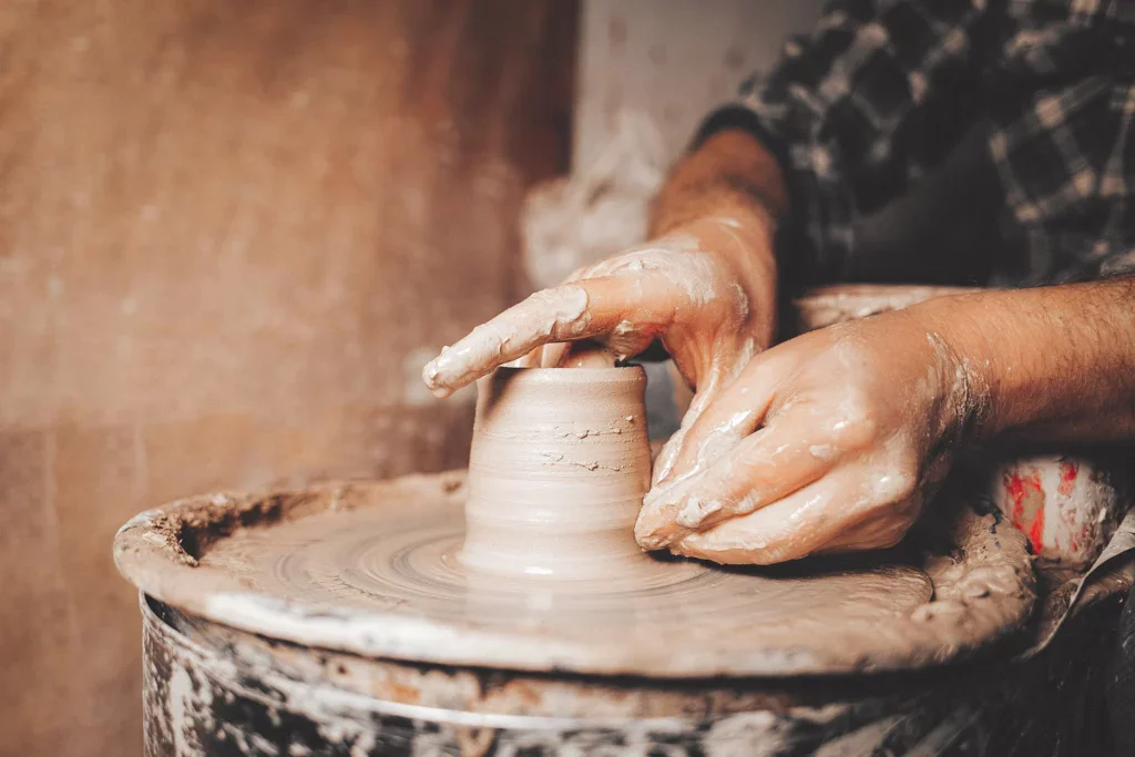 Pottenbakken benodigdheden: een man aan de draaischijf trekt de wanden van een pot op