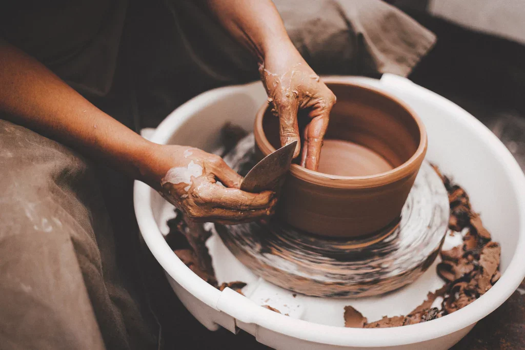 een persoon aan de draaischijf in het keramiek atelier tijdens de het afdraaien van een kom met een lomer