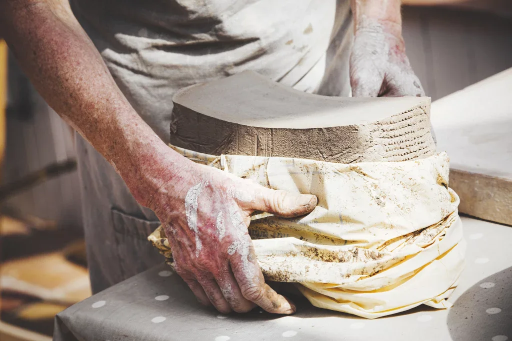 Een persoon haalt een groot pak klei uit de verpakking in het klei atelier, klei bewaren
