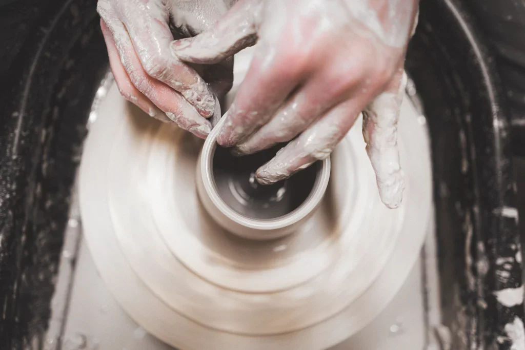 Two hands are pulling up the clay at the potter's wheel