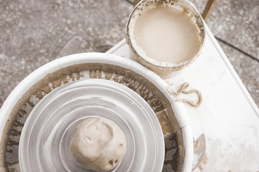 Een bol klei op het midden van een draaischijf en een emmer slib