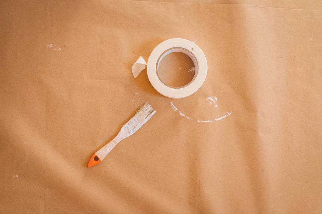 Afdekken met tape: rol witte schilderstape en verfborstel op ondergrond van bruin papier