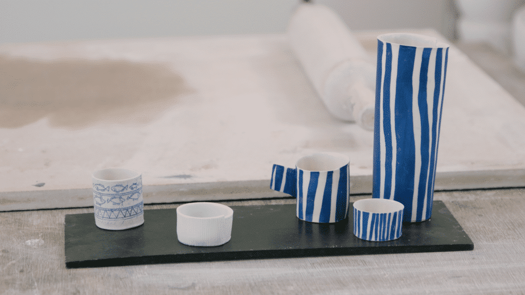 Vlasklei: zwarte plank met witte tassen en vaasjes op klein en groot met blauwe gekronkelde strepen