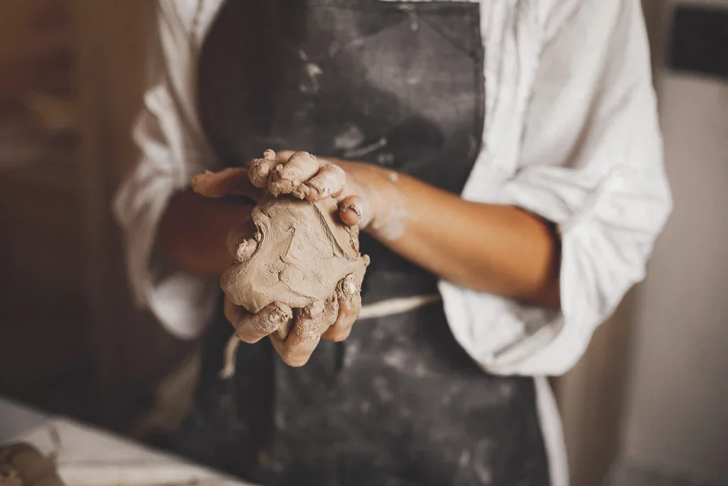 Persoon met bol klei in handen en keramiek kleren