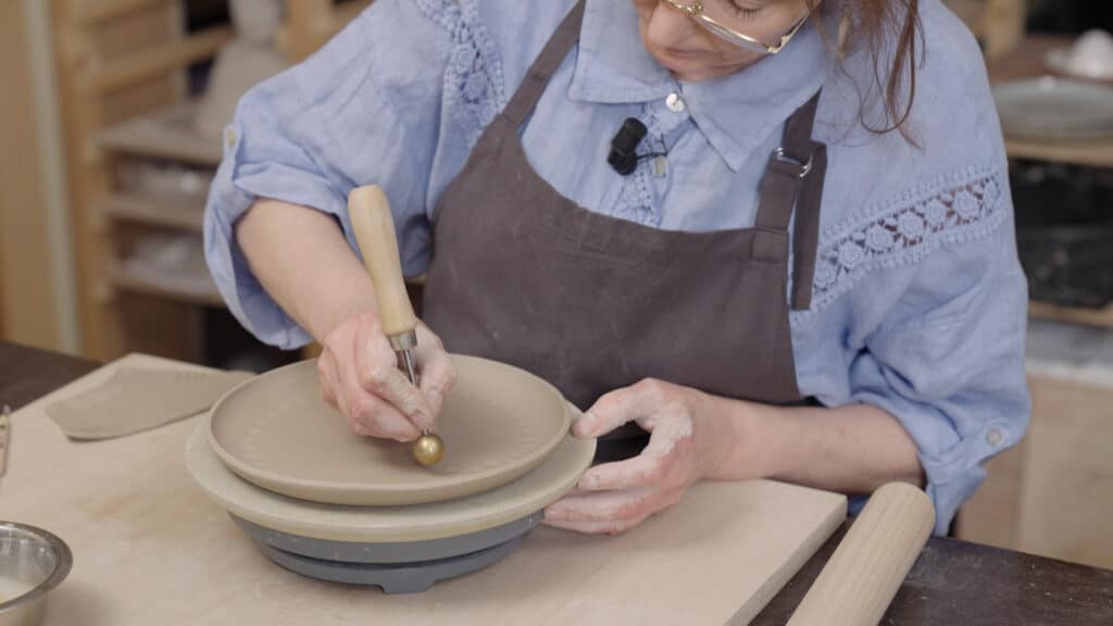 Zelf keramiek maken: Kathleen zit met tool in bruin bord uit de mal