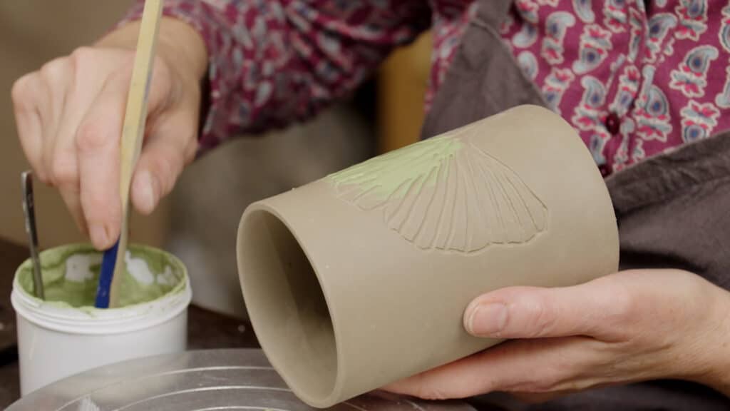 Zelf keramiek maken: intarsia, schilderen met groen slib op bruine cilinder vorm
