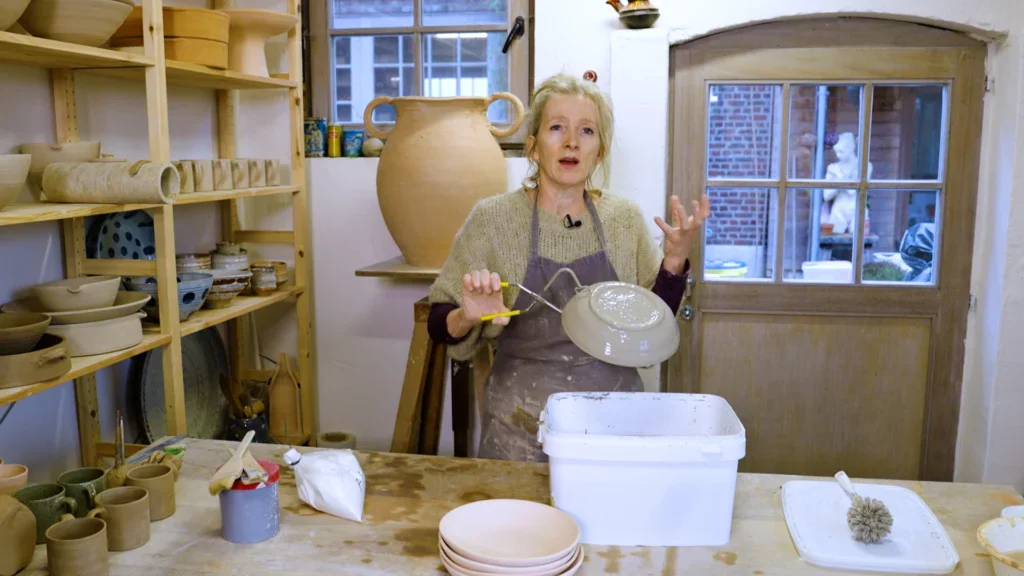 Aster Caemaert dompelt kleivorm in glazuur met een tang bij het klei draaien