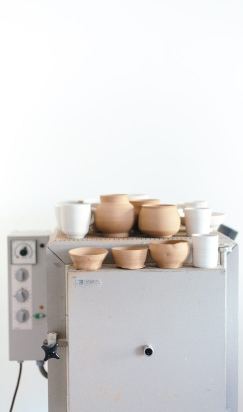 Een grijze keramiekoven voor een witte muur met op de bovenkant potjes in rode en witte klei